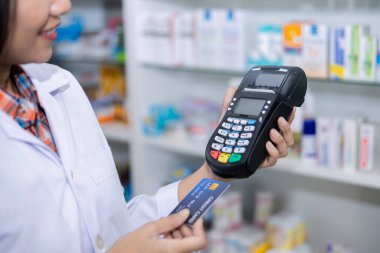 Eczacı Asyalı kadın eczacı ve kredi kartı makinesi sağlık ve dijital ödeme konsepti Tayland spor odağı bulanık arka plan