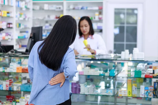 female patient standing in back pharmacy with doctor and shelf medicine background