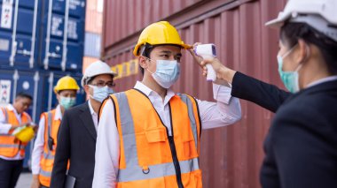 Mühendis kadınlar dijital termometreyi tutuyor, yüz maskesi takan ekran işçileri için sıcaklık ölçüyor, Covid-19 salgınını önlüyor, imalat fabrikasındaki sanayi mühendisleri sırada bekliyor. Tayland 