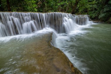 Hua Mea Khamin Şelalesi 'nde tropikal ağaçlar, eğrelti otları sabah ışığında şelalede büyüyen serin, temiz hava ve ormanda dinlenmek için sakin bir yer vardır. Karnchanaburi, Tayland.