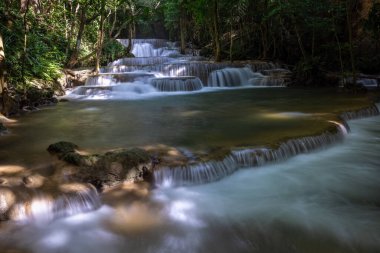 Hua Mea Khamin Şelalesi 'nde tropikal ağaçlar, eğrelti otları sabah ışığında şelalede büyüyen serin, temiz hava ve ormanda dinlenmek için sakin bir yer vardır. Karnchanaburi, Tayland.