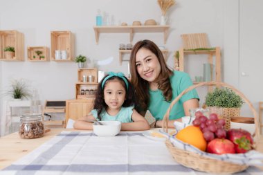 İki anne ve kız kahvaltı ve meyveyle mutfak masasında oturuyorlar.