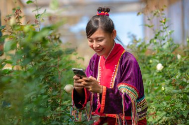 Karen 'ın elbisesi içindeki genç kadın telefon kamerasını kullanarak Tayland' ın gül bahçesinde Rose 'un fotoğraflarını çekiyor.