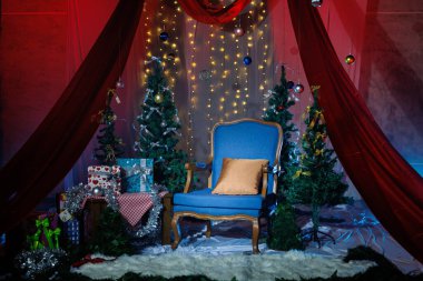 Gece vakti, Noel temalı oturma odası dekorasyonu. Mavi eski koltuklar, kırmızı perdeler, Noel ağaçları ve Bokeh perisi ışıklarıyla hediye kutuları..