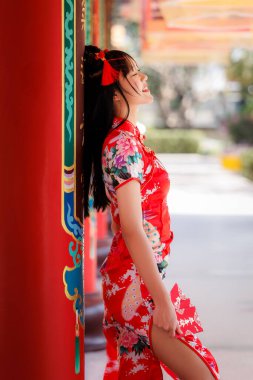 Geleneksel Çin kıyafetleri içinde mutlu bir kadının açık havada bayramı kutlamasının yan profili yumuşak doğal ışık onun dingin ifadesini ve canlı kırmızı qipao 'sunu vurguluyor.