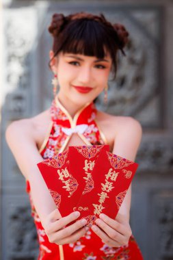 Çifte çörek saç stiline sahip gülümseyen genç bir kadın, iyi şans ve refahı simgeleyen kırmızı Hongbao zarfları sunarak Ay 'ın yeni yıl geleneğini kutluyor.