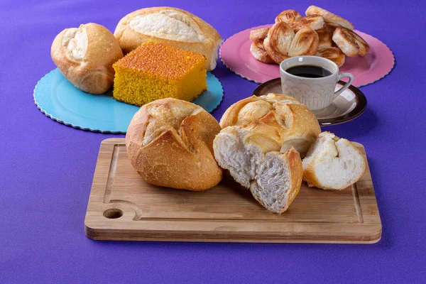 Ahşap bir tahtanın üzerinde fırın tatlıları, arka planda havuçlu kek ve bir fincan kahvenin yanında Fransız ekmeği. Hepsi desenli mor bir arka planda.