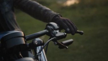 Debriyaj kolunu iten siyah eldivenli bir motorcunun eline yakın çekim. Macera, seyahat, yolculuk. Arkaplanda orman.