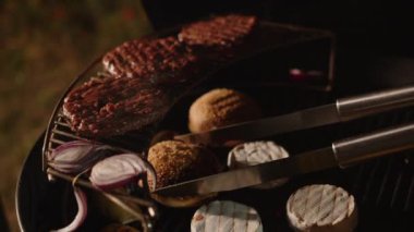 Hamburger çörekleri, Camembert peyniri ve sulu sığır pirzolası ızgarada pişiriliyor. Maşa kapanışı, ızgara yemek..