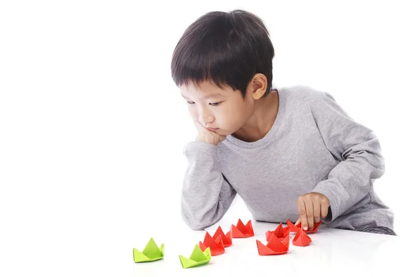 Концентрированный мальчик играет на бумажных кораблях на столе — стоковое фото