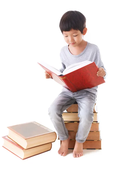 Азиатский милый мальчик читает книгу, сидя на стопке книг. whi — стоковое фото
