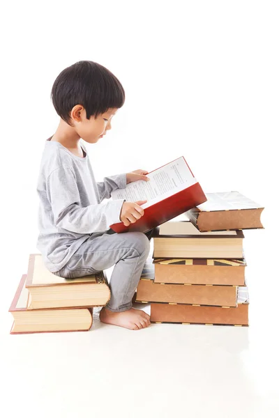 Asian cute boy reading book while sitting on stack of books. whi — Stock Photo, Image