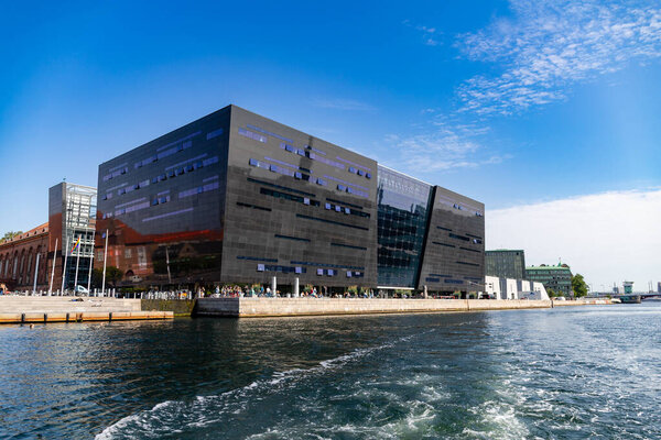 Копенгаген, Дания-14 августа 2025: Черный бриллиант, часть Королевской датской библиотеки, отражает солнце и городской пейзаж вдоль набережной гавани под ясным голубым небом.