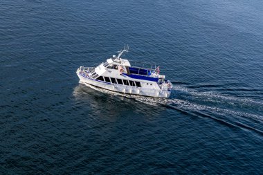 Kristiansand, Norveç-12 Ağustos 2025: Norveç bayrağı taşıyan beyaz-mavi gezi teknesi güneşli bir yaz gününde sakin fiyort sularında hareket ediyor.