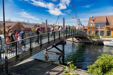 Kristiansand, Norveç-12 Ağustos 2025: Kristiansand 'da renkli binalar ve yolcu gemisiyle küçük kemerli ahşap bir köprüden geçen kalabalık.