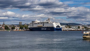 Oslo, Norveç-11 Ağustos 2025: Büyük Renk Hattı yolcu gemisi şehir limanına kentli silueti ve bulutlu arka planıyla kenetlendi.