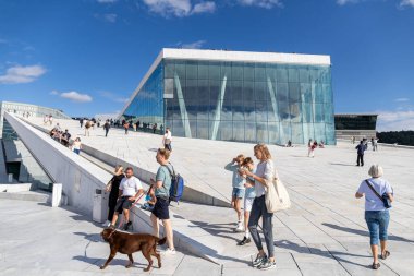 Oslo, Norveç-11 Ağustos 2025: Aileler, turistler ve köpek gezginleri, Oslo Operası 'nın eğimli beyaz mermer yüzeyinde berrak bir gökyüzünün altında dinleniyorlar.
