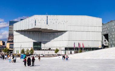 Oslo, Norveç-11 Ağustos 2025: İnsanlar Oslo Merkez İstasyonu yakınlarındaki Deichman Kütüphanesi 'nde modern cam cephe ve ön planda bayraklarla yürüyor.