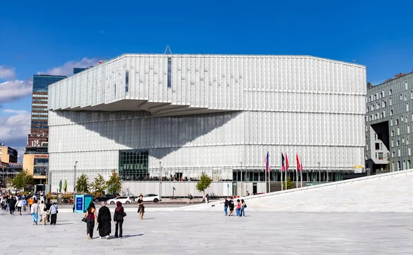 Oslo, Norveç-11 Ağustos 2025: İnsanlar Oslo Merkez İstasyonu yakınlarındaki Deichman Kütüphanesi 'nde modern cam cephe ve ön planda bayraklarla yürüyor.