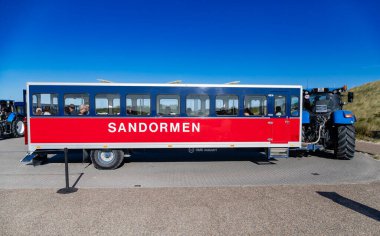 Grenen, Danimarka çirkinliği 8, 2025: Mavi bir traktör tarafından çekilen Sandormen mekiğinin yan görüntüsü, ziyaretçileri Skagen 'in manzaralı kum tepelerinden geçiriyor..