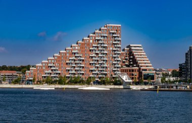 Aarhus, Danimarka-15 Ağustos 2025: Limandaki benzersiz kırmızı tuğlalı apartman, modern tasarım, sudaki wakeboard engelleri.