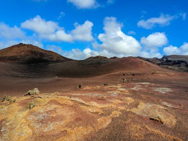İspanya, Kanarya Adaları, Lanzarote-6 Şubat 2026: Dramatik bulutların altında eşsiz lav dokuları olan kırmızı ve kahverengi volkanik tepeler.