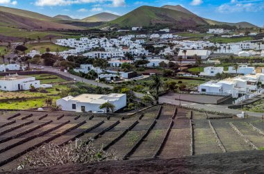 İspanya, Kanarya Adaları, Lanzarote-6 Şubat 2026: Teraslı volkanik alanlar ve yeşil tepelerin altında beyaz köy evleri ve gezici fotoğraf olarak belgelenmiş bulutlu mavi gökyüzü.