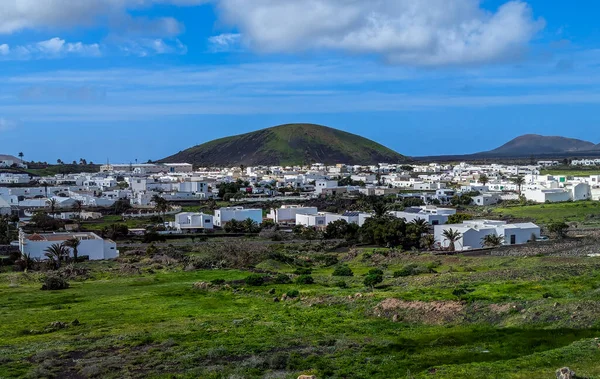 İspanya, Kanarya Adaları, Lanzarote-6 Şubat 2026: Beyaz köy, Atlantik kıyısındaki yeşil volkanik tepenin altında, parlak mavi gökyüzünün altında gezici manzara fotoğrafı olarak ele geçirildi..