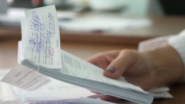 Ofisteki genç bir kadının elinde bir paket kamu hizmetleri makbuzu. Geniş bir ofisteki masada oturan genç bir kadının makyajlı, bakımlı bir kadın elinin bir paket kamu hizmetleri makbuzunun etkileyici yakın çekimi..