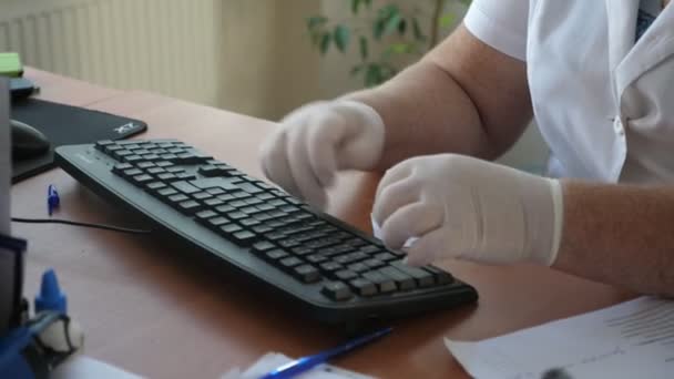 医療従事者が座って ゴム手袋でコンピュータキーボードに印刷する女性医療従事者の元の閉鎖は 風通しの良いオフィスでゴム手袋でコンピュータキーボードに座って印刷します それはプロと罰金に見えます — ストック動画