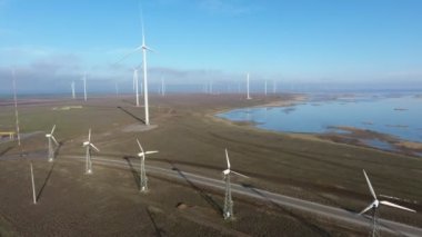 Yazın dönen bıçaklarla rüzgar enerjisi direklerinin hava görüntüsü neşeli kuş bakışı bir sıra yükselen beyaz sütunlar ve dönen bıçaklarla yazın güneşli bir günde rüzgâr enerjisi topluyor. Deniz kenarı güzel görünüyor..