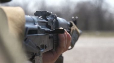 Ateşleme sahasında AK-74 'ten ateşlenen bir asker ve yazın uçan bir kartuş. Askeri Bokeh, yazın güneşli bir günde ağır çekimde, AK-74 'ten ateşlenen bir askerin üzerine havai fişekle attığı yakın çekim..