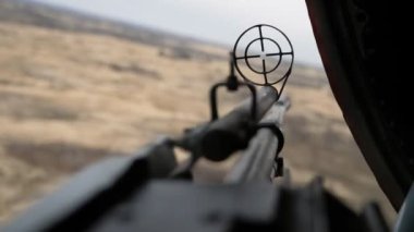 Yazın uçan bir helikopterin kapağına bakan yuvarlak görüşlü bir makineli tüfek. Yazın güneşli bir günde askeri helikopterin kapağına bakan modern bir makineli tüfek. Sarı bozkır arkada görünüyor.