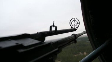Yazın hareket halindeki bir helikopterin MI-8 kapağından sarkan yuvarlak görüşlü makineli tüfek. Güneşli bir yaz gününde ormanın üzerinde uçan askeri helikopterin camına bakarak modernize edilmiş makineli tüfeğin görkemli görüntüsü.