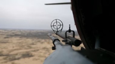 Modern makineli tüfek, kartuş bandıyla çölü kontrol ediyor. 12.7 mm 'lik makineli tüfek, titreyen kartuş bandı ve yuvarlak görüşlü. Bahar havasında uçan helikopterde çöl hedeflerini kontrol ediyor..