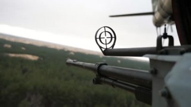 Bulutlu baharda uçan bir helikoptere yerleştirilmiş kartuş bantlı bellikoz makineli tüfek bahar havasında helikopterle uçan orman nesnelerine sabitlenmiş 12.7 mm 'lik bir makineli tüfeğin harika görüntüsü. Savunmaya geçmiş gibi görünüyor..