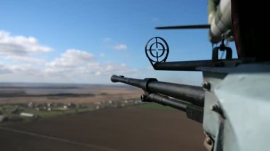 Yuvarlak görüşlü büyük makineli tüfek, baharda bulutlu bir havada uçan bir helikopterin taşıdığı kara cisimlerini hedef alan geniş ve modern bir makineli tüfeğin görüntüsünü taşıyan bir helikopterden karaya hedeflenir.
