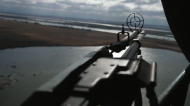 Yuvarlak görüşlü büyük makineli tüfek, baharda bulutlu bir havada uçan bir helikopterin taşıdığı bir göl ile manzarayı hedefleyen büyük ve modern bir makineli tüfeğin olduğu bir helikopterden göle nişan alınıyor.
