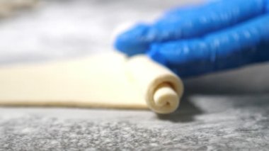 Fırında kruvasan şekillendirmek için eldivenli kadın eller kauçuk eldivenli işçilerin ellerinin metal bir masada hamurdan bir çarşaf sararak bir fırın fabrikasında kruvasan yapmasını sağlıyor. İyi görünüyor.