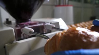 Pastanedeki iki metal çubuktan reçel dolduran taze kruvasanlar sıcak ve lezzetli kruvasanların, fırında lastik eldivenler giymiş bir işçinin ellerinde tutulan iki metal çubuktan reçel dolduruşunu hayret verici bir şekilde görüyorlar..