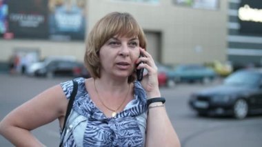 Baharda, şehrin bir sokağında telefonla konuşan gülümseyen bir kadın. Yavaş çekimde başarılı sarışın bir kadının, şık bir elbiseyle, şehrin kalabalık bir sokağında, akıllı telefonuyla sohbet edişinin muhteşem görüntüsüyle. Arkasında modern otomobiller var.