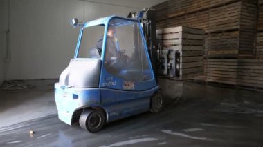 Küçük forklift, sebzelerle ahşap paletleri büyük bir depoda taşır. Küçük bir forklift, sebzelerle ahşap paletleri hareket ettiren ve yüksek tavanlı tarım ürünleri üreten yüksek raflara yerleştirir.