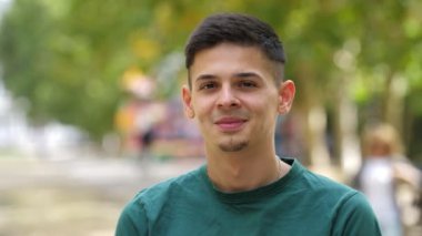 Yazın, yeşil tişörtlü, ayakta duran ve sırıtan genç bir adam kısa saçlı, yeşil tişörtlü ve yazın bir sokakta gülümseyen genç bir esmer adamı cesaretlendiriyor. Mutlu ve iyimser görünüyor..