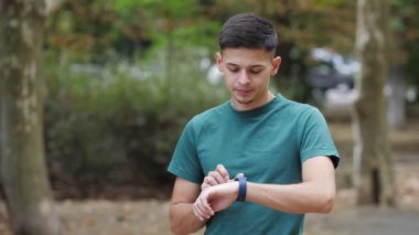 Başarılı bir adam yeşil caddedeki kol saatindeki saati düzeltir. Yeşil tişörtlü genç bir adam kolunda plastik bir bilezik olan saatini ayarlar. Caddedeki ekrana dokunuyor..