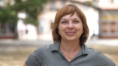 Güzel saçlı bir kadın, yeşil bir parkta, yazın eğleniyor ve gülümsüyor. Gri bluzlu, kısa saçlı, neşeli, sarışın bir kadın yaz mevsiminde güneşli bir parka bakıyor ve gülümsüyor..