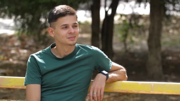 Jovem Feliz Sentado Banco Sorrindo Olhando Para Lado Parque Verão — Vídeo de Stock