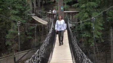 Karpatlar 'da asma bir köprüde nakışlı gömlekli neşeli bir kadın. Karpatlar' da yaz aylarında süslenmiş gömlek giymiş, ahşap asma köprüde yürüyen, kısa saçlı, gülümseyen, sarışın bir kadının heycanlı görüntüsü.. 