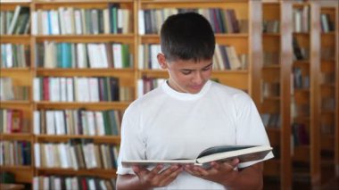 Kütüphanede kameraya bakarak ve gülümseyen bir okul çocuğu