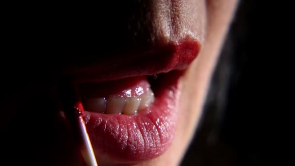 Frau bemalt ihre Lippen mit Lippenstift auf schwarzem Hintergrund, Nahaufnahme — Stockvideo