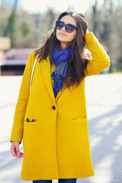 Jonge brunette vrouw in een gele vacht en zonnebril corrigeert ha — Stockfoto